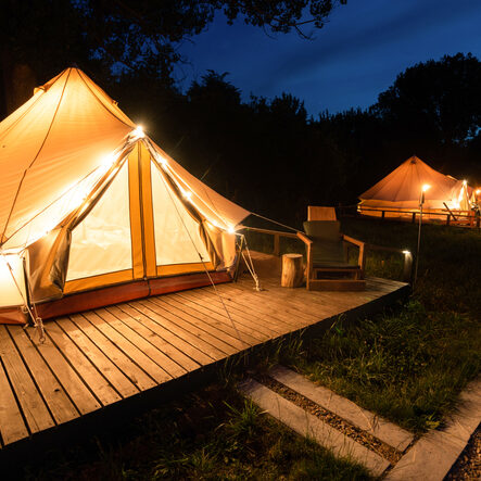 rezStream Glamping Software Glamping tents with burning torches, lamps and wooden chairs at glamping, forest around, night