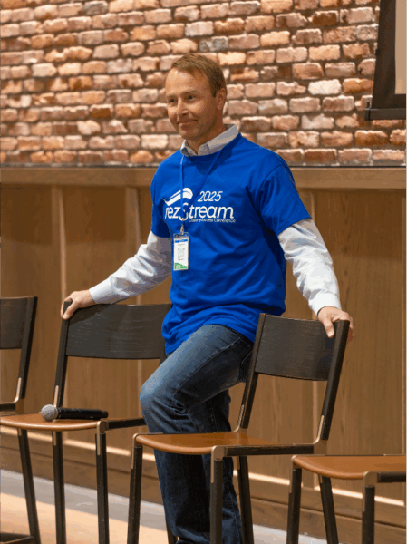 Christian Holmsen, CEO of rezStream, smiling and leaning on a chair while delivering opening remarks at the 2025 Customer Success Conference.